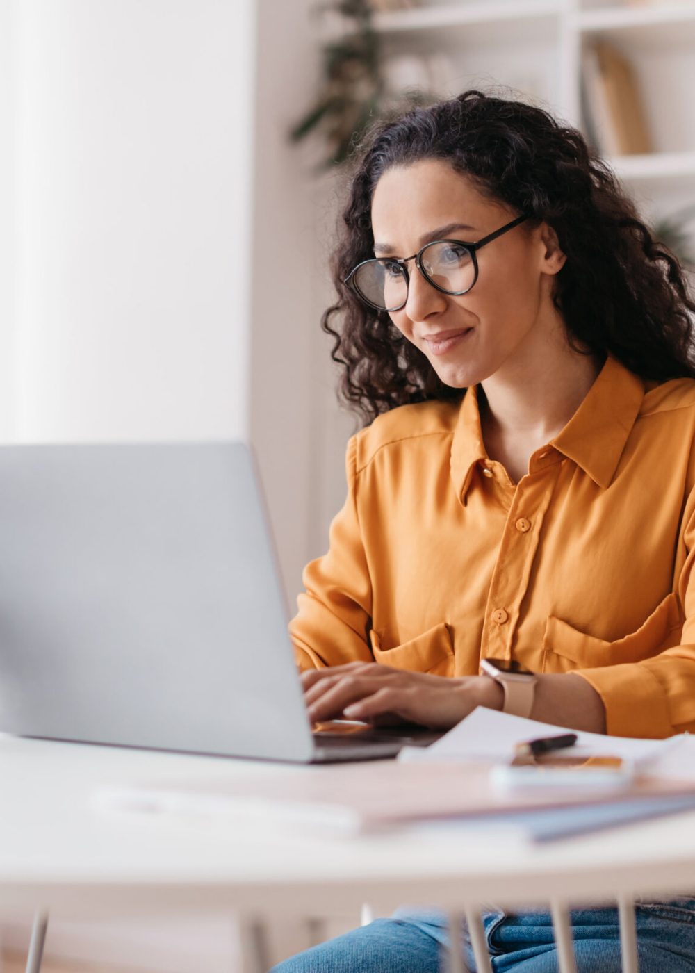 Middle Eastern Lady Using Laptop Working Online Wearing Eyewear Sitting At Workplace In Modern Office. Remote Job, Technology And Career Profession Concept. Side View